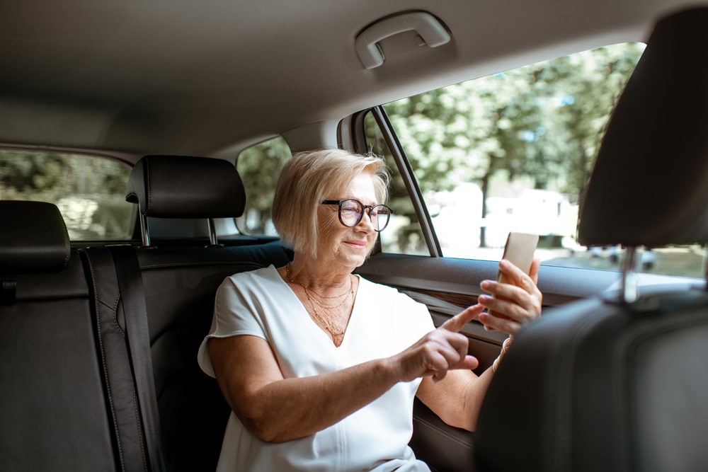 Senior business woman talking with phone while sitting on the back seat in the modern car. Concept of a business life on retirement